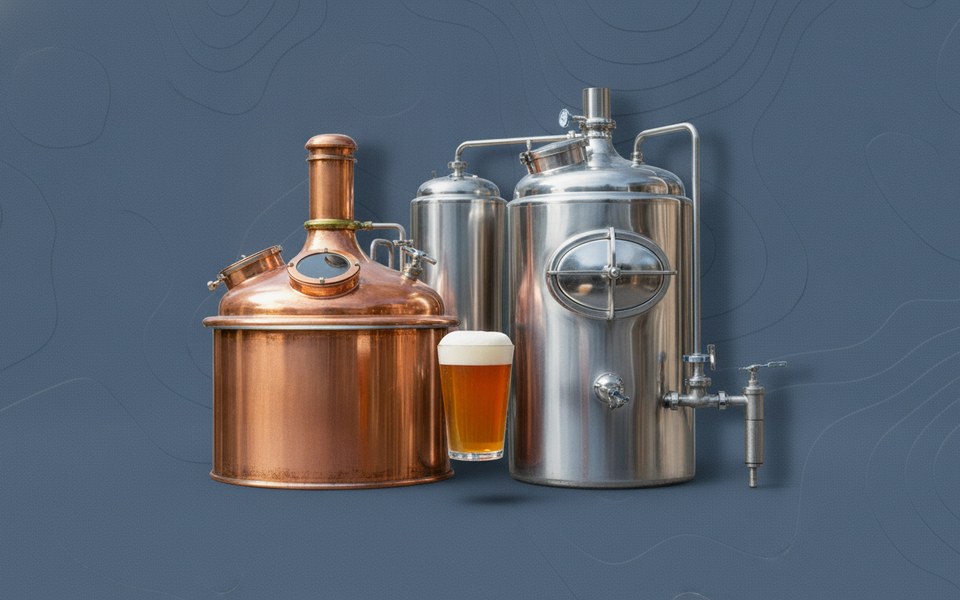 Copper and stainless steel craft brewing tanks beside a glass of amber beer